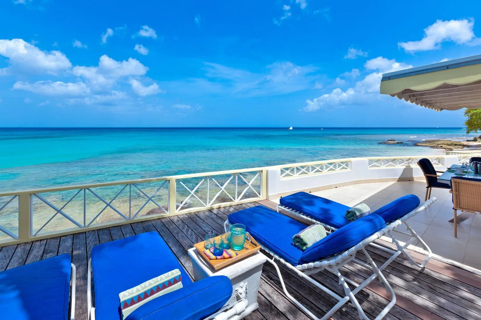 A seaside deck with blue lounge seating overlooks clear turquoise water.