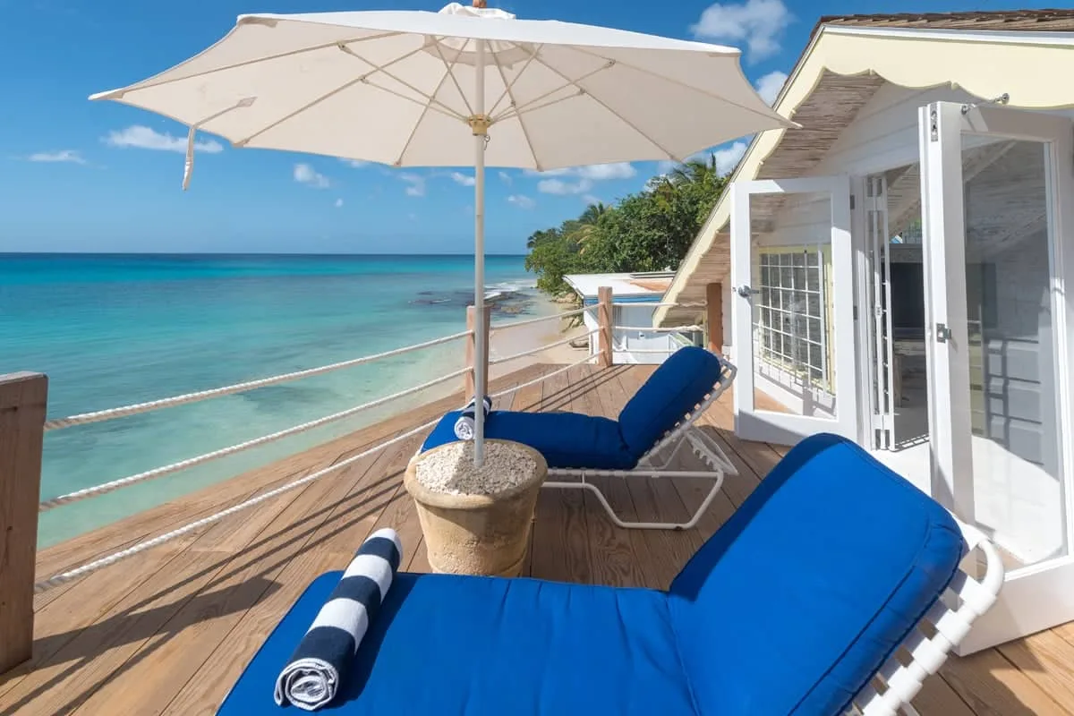 A wooden seaside deck with blue lounge seating and a large sun umbrella.