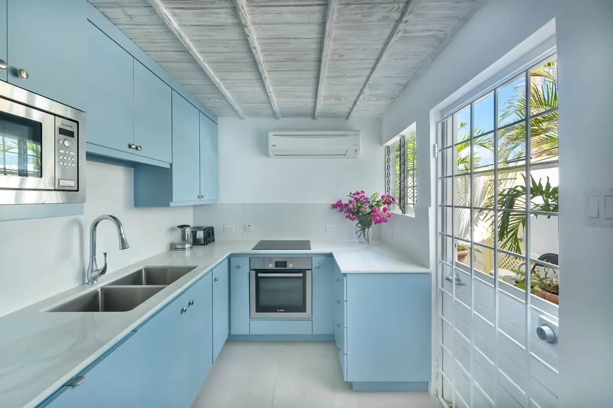 A bright kitchen with pale blue cabinets and a countertop along the windows.