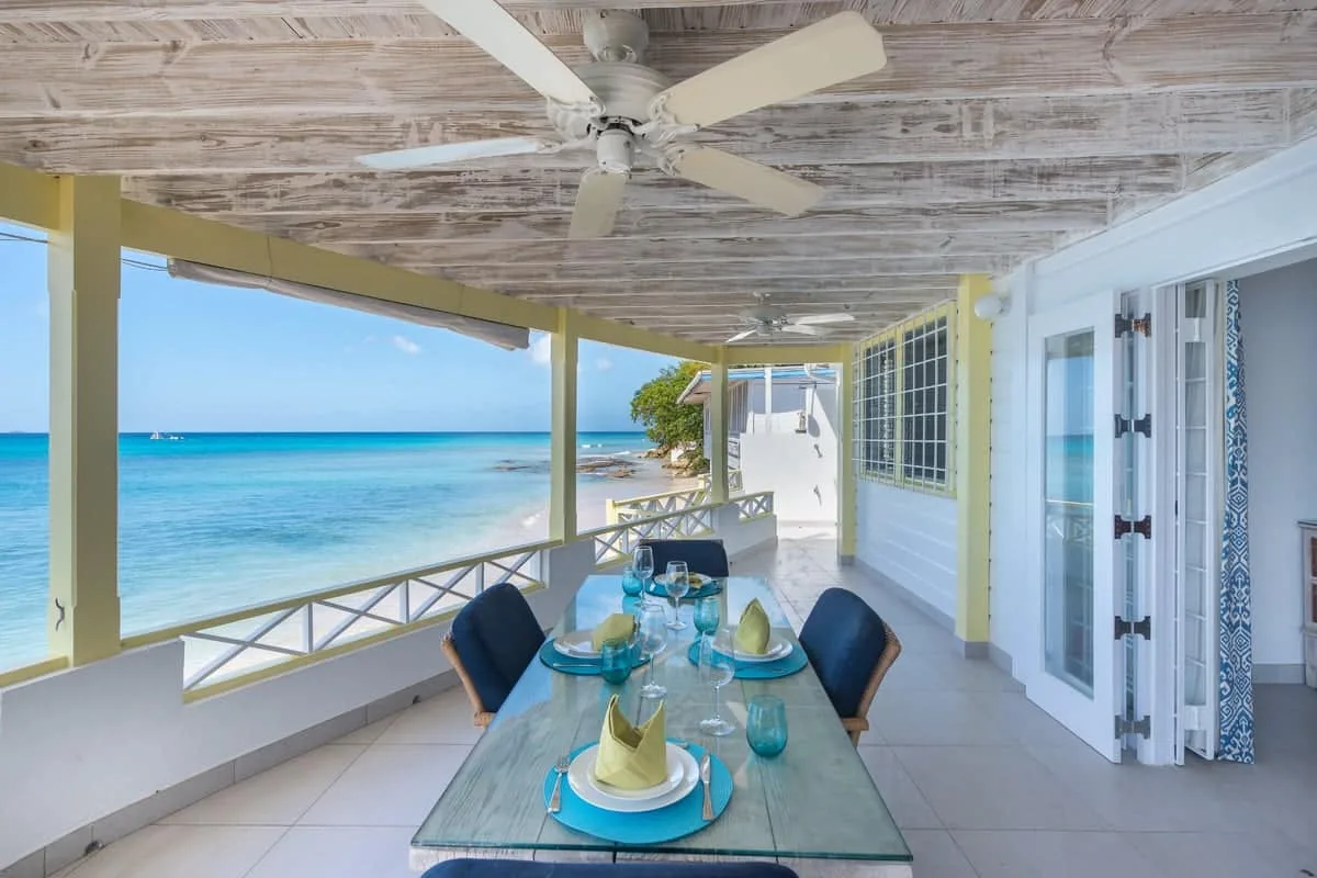 A covered seaside dining area overlooks the ocean, with a table and chairs.