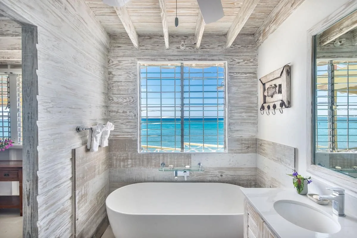 A bright bathroom with a bathtub and a window overlooking the ocean.