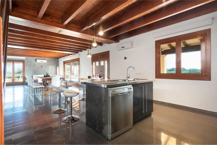 Una luminosa cocina-comedor abierta con encimeras oscuras y vigas de madera a la vista.