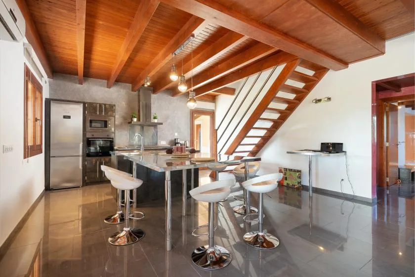 Una cocina y zona de comedor abiertas están bajo una escalera de madera y vigas expuestas.