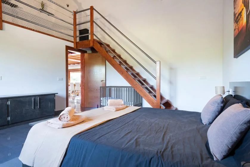 Un dormitorio con una cama bajo una escalera de madera y una barandilla de altillo.