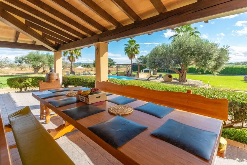 Una zona de comedor exterior cubierta da a un jardín y una piscina.