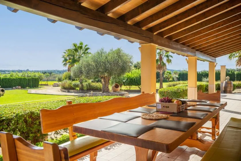 Un comedor exterior cubierto con una mesa larga y vistas a un jardín cuidado.