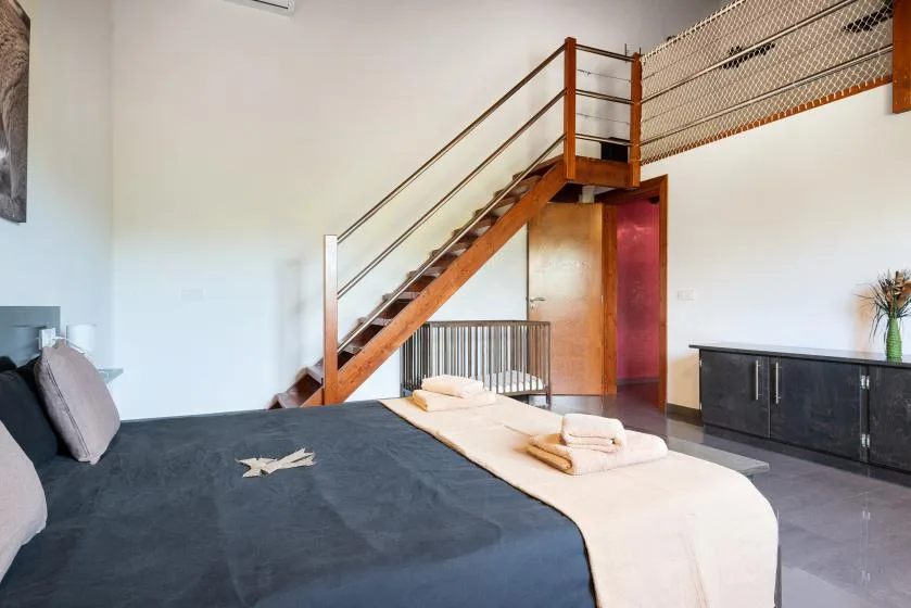 Un dormitorio con una cama bajo una escalera de madera y un armario oscuro.