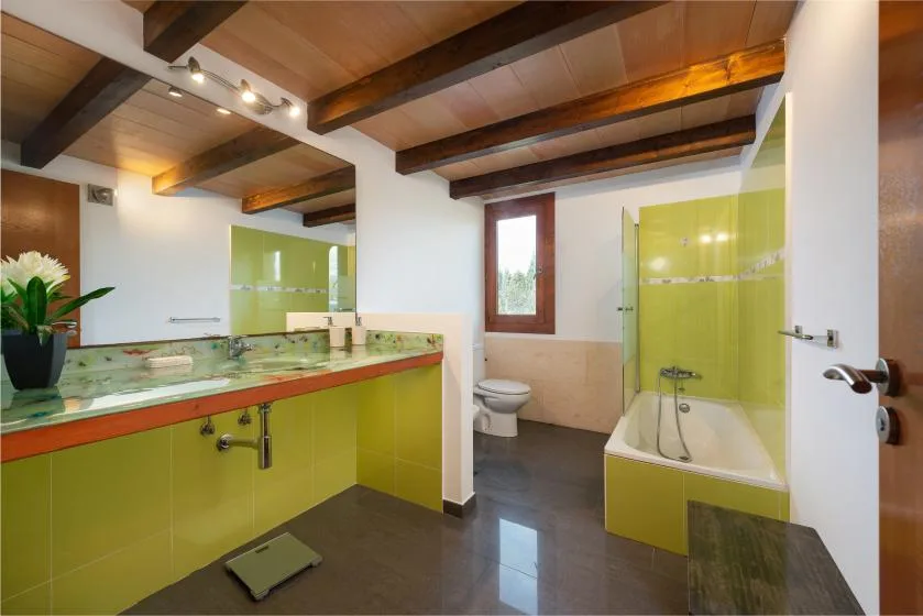 Un baño con un lavabo revestido de verde y una bañera bajo vigas expuestas.
