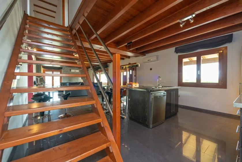 Una escalera abierta de madera da a una cocina con isla y una ventana.