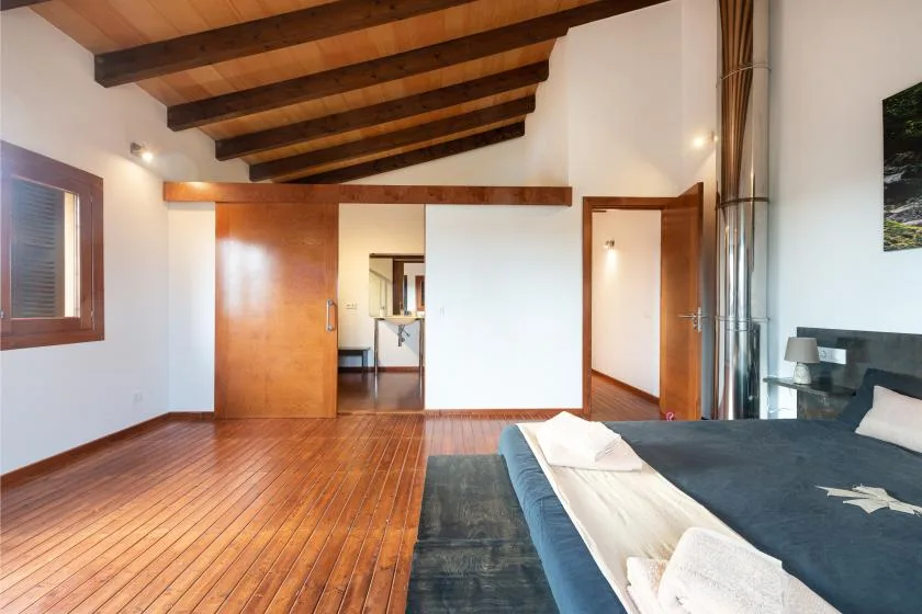 Un dormitorio con una cama, suelo de madera y vigas expuestas en el techo.