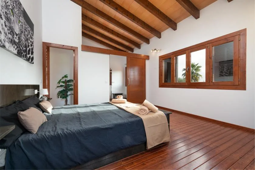 Un dormitorio con una cama bajo vigas de madera vistas y una ventana amplia.