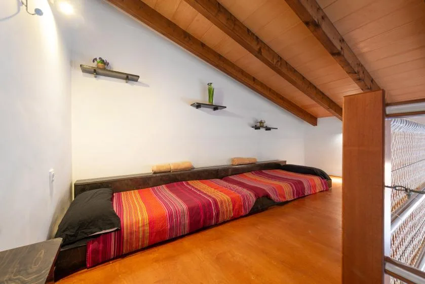 Una zona para dormir con una cama colorida bajo un techo inclinado de madera.