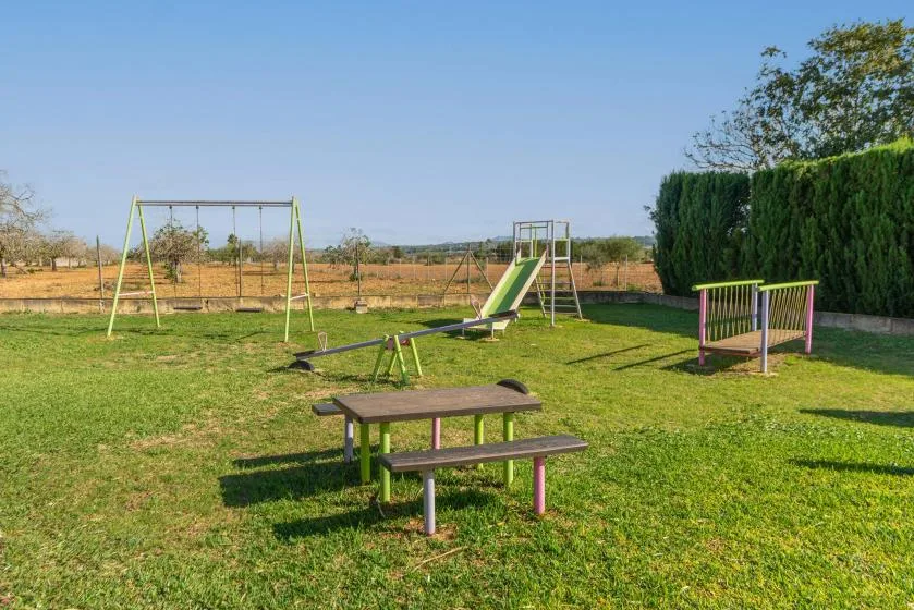 Un parque infantil al aire libre con tobogán, columpios y una mesa de picnic sobre el césped.