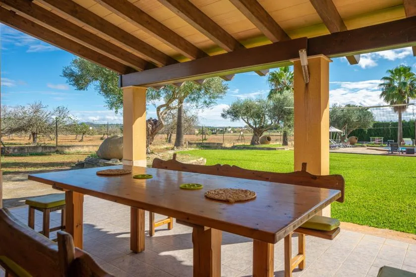 Comedor exterior cubierto con una mesa larga de madera frente a un césped verde.