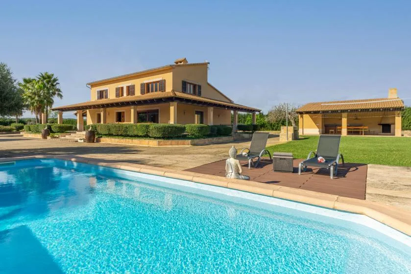 Una piscina junto a una casa grande, con asientos reclinables en la terraza.