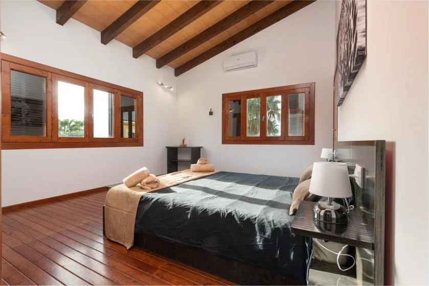 Un dormitorio con una cama bajo vigas de madera expuestas y ventanas.
