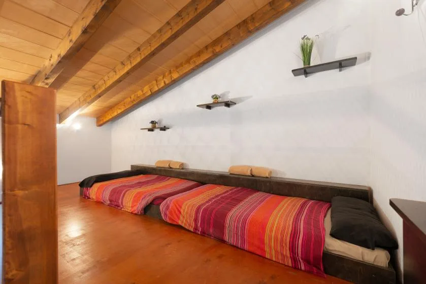 Un dormitorio con una cama baja cubierta con una manta de rayas coloridas bajo un techo de madera inclinado.