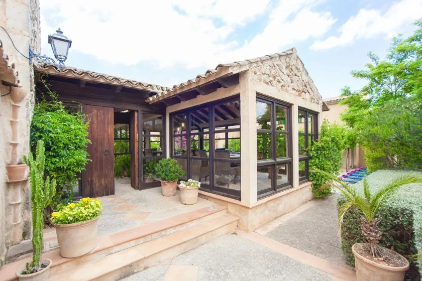 Un patio acristalado junto a un edificio de piedra, con plantas en macetas y jardín.