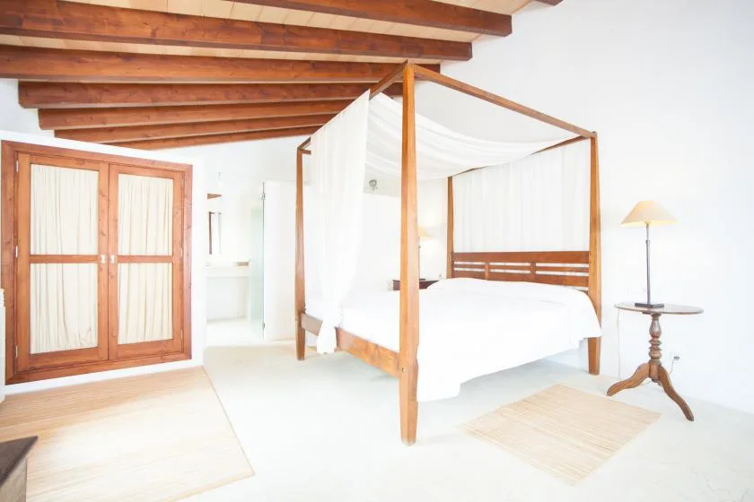 Un dormitorio luminoso con una cama con dosel de madera y vigas expuestas.