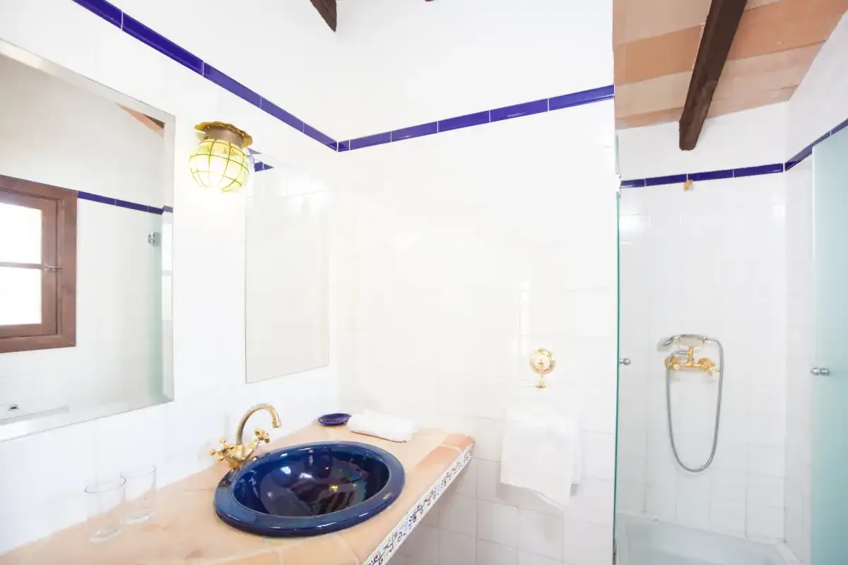 Un baño luminoso con azulejos, lavabo azul y ducha de cristal.