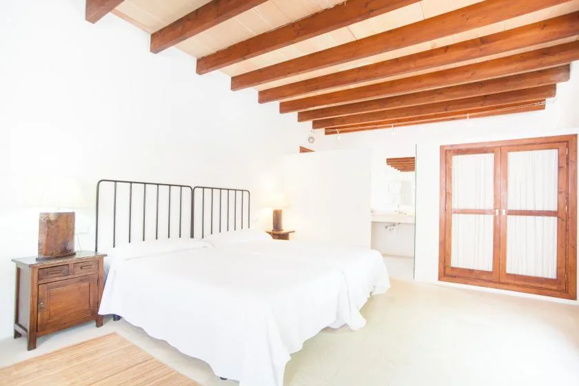 Un dormitorio luminoso con una cama blanca bajo vigas de madera expuestas.