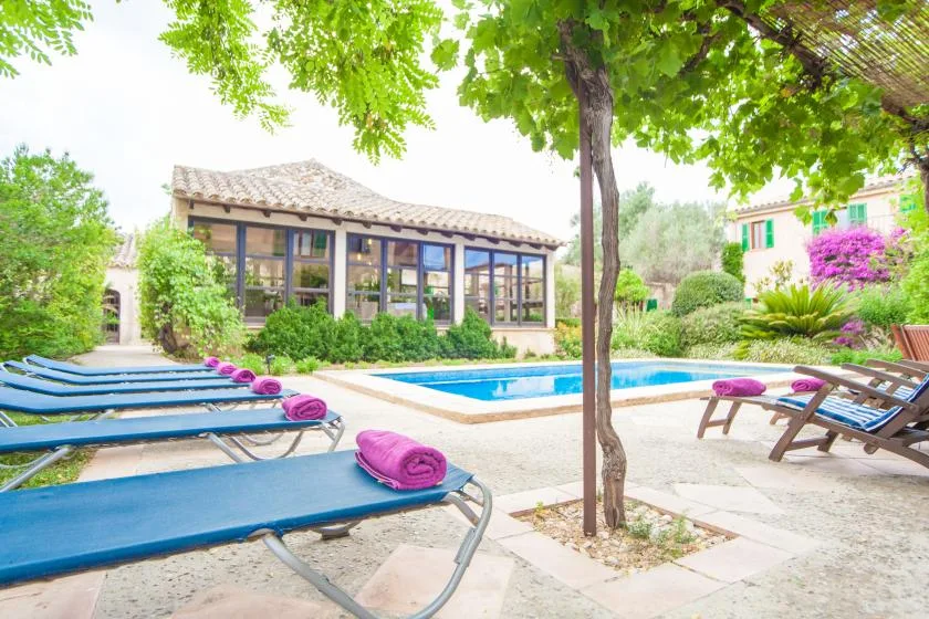 Una piscina al aire libre junto a un edificio con fachada acristalada y asientos de descanso.