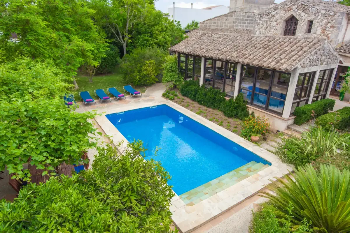 Una piscina junto a un edificio de piedra, rodeada de vegetación y tumbonas.