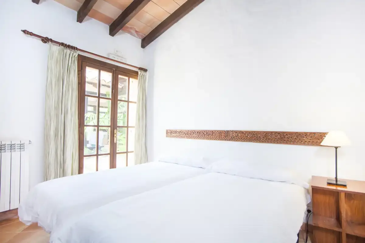Un dormitorio con una cama, una ventana con cortinas y vigas de techo vistas.