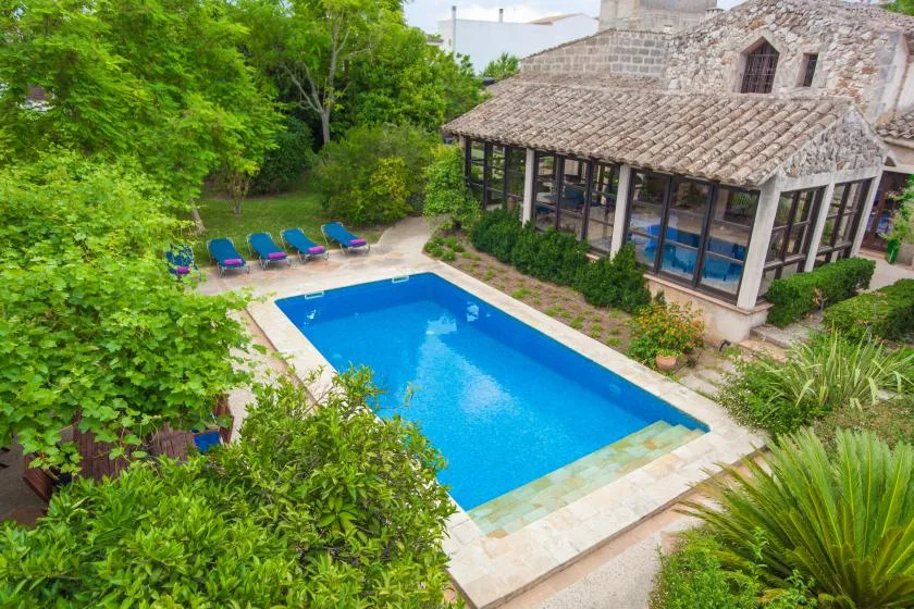 Una piscina al aire libre junto a una zona de estar cubierta y vegetación.