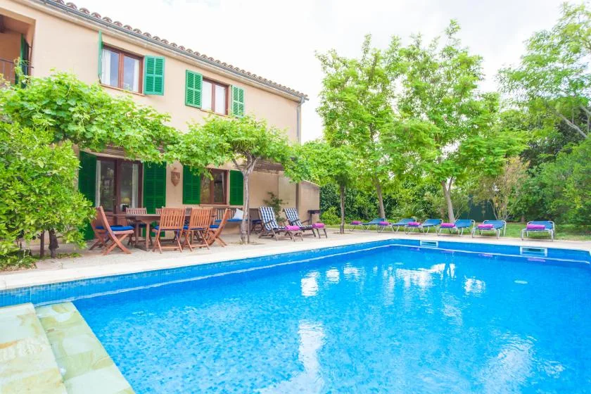 Una piscina al aire libre junto a una casa y un patio arbolado.