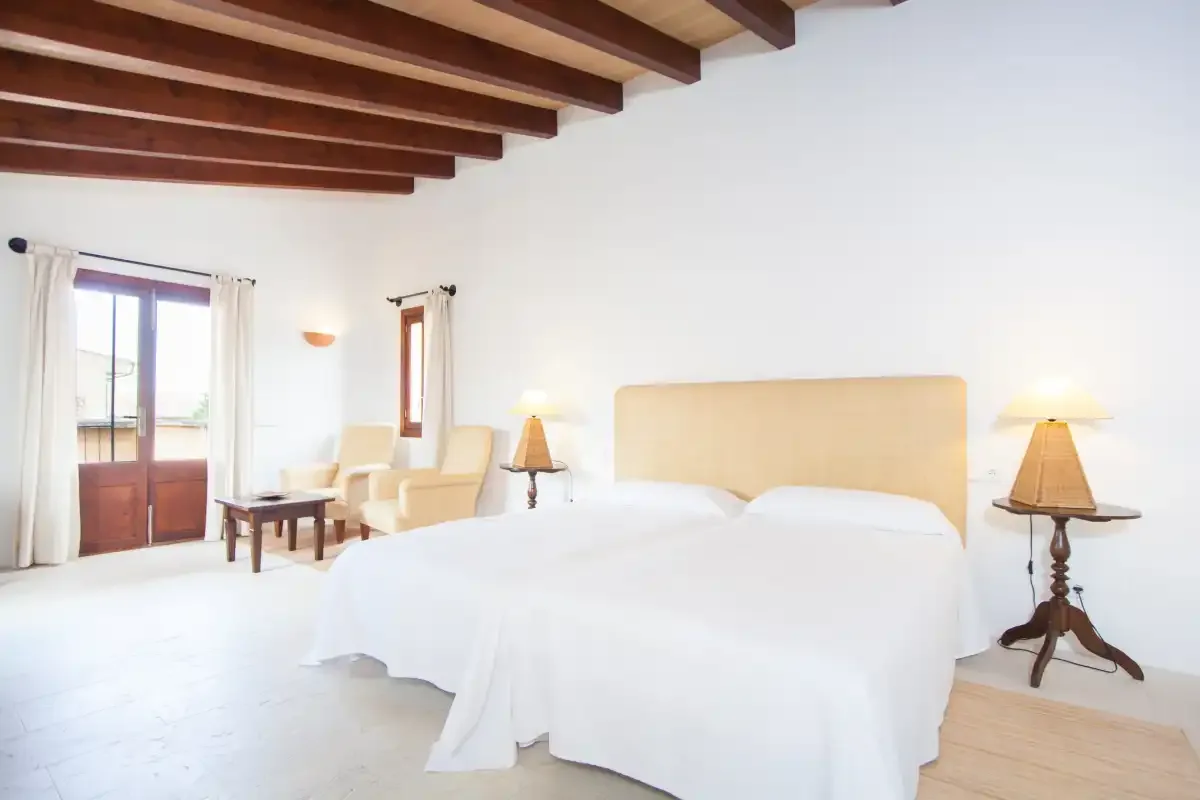 Un dormitorio luminoso con una cama grande, lámparas de noche y vigas de madera vistas.