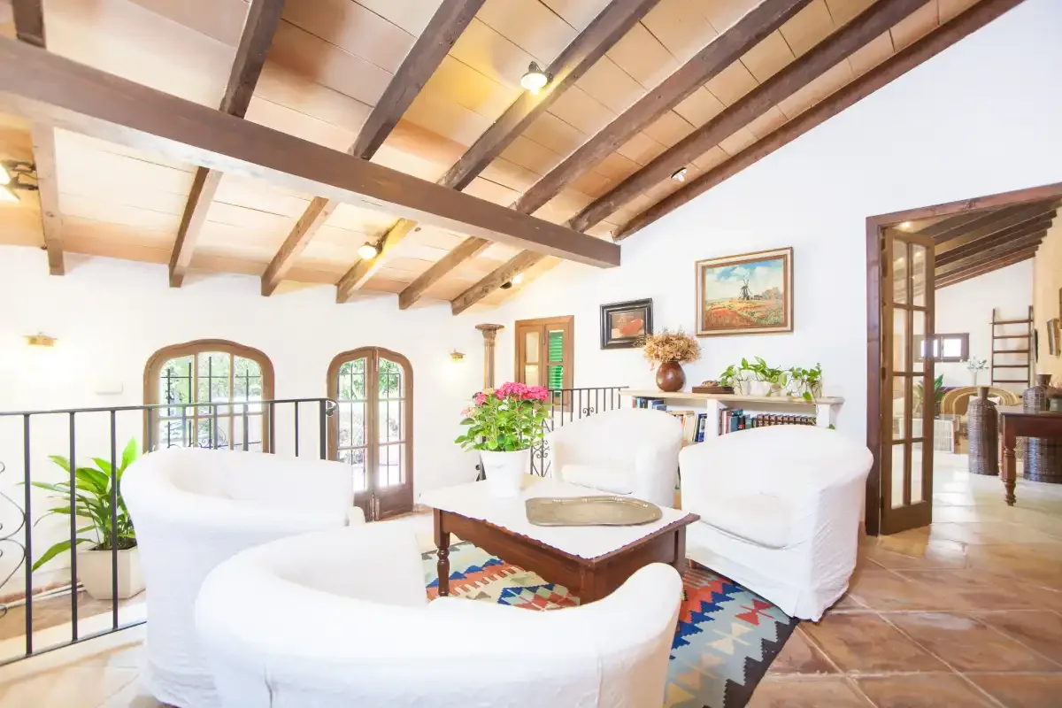 Una luminosa sala de estar con asientos blancos, una mesa de centro y vigas expuestas.