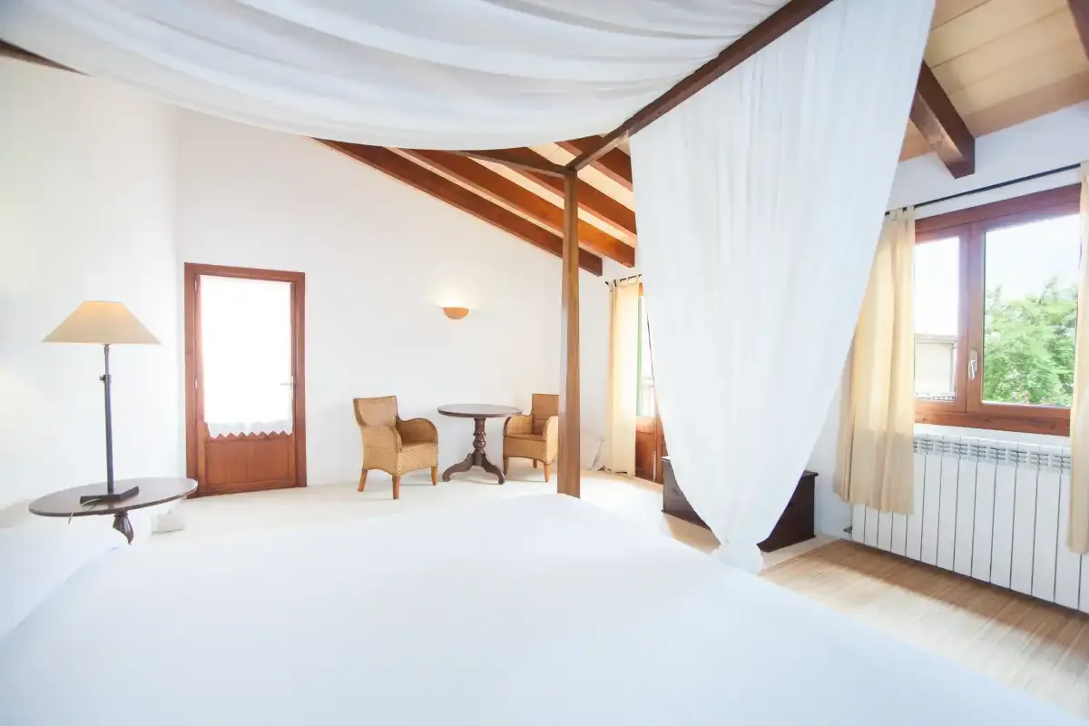 Un dormitorio luminoso con dosel drapeado y una pequeña zona de estar junto a la ventana.