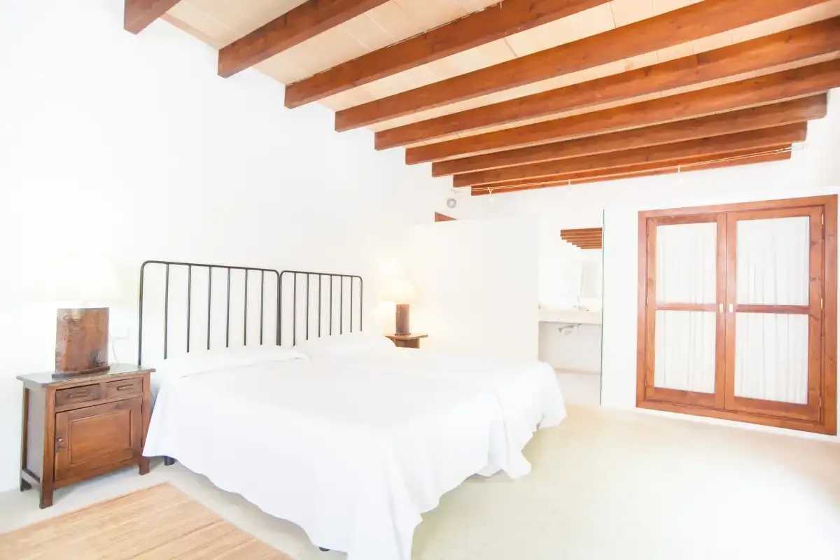 Un dormitorio luminoso con una cama blanca, vigas de madera vistas y puertas de cristal.