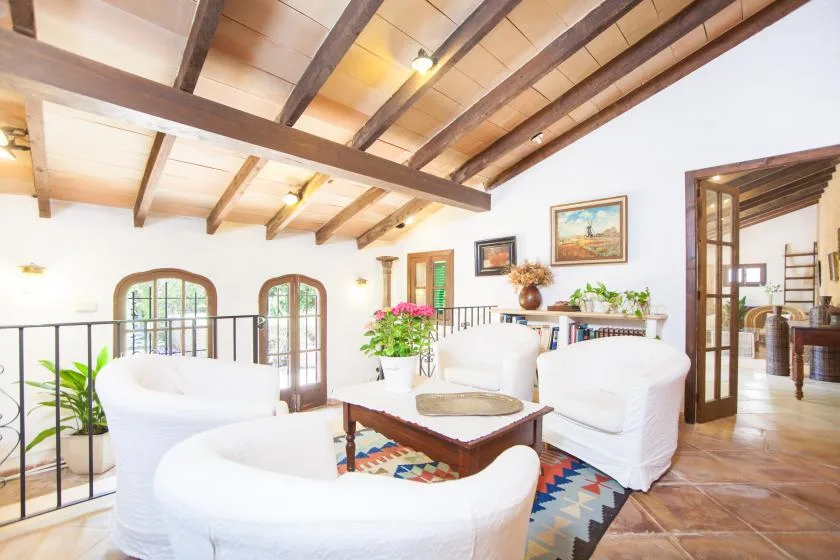 Una sala luminosa con asientos blancos, una mesa de centro y vigas de madera expuestas en el techo.
