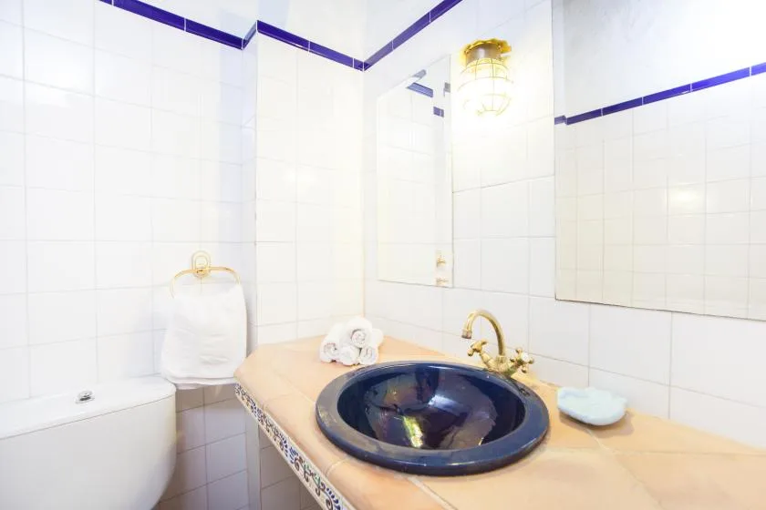 Un lavabo de baño alicatado con un fregadero oscuro y un espejo.