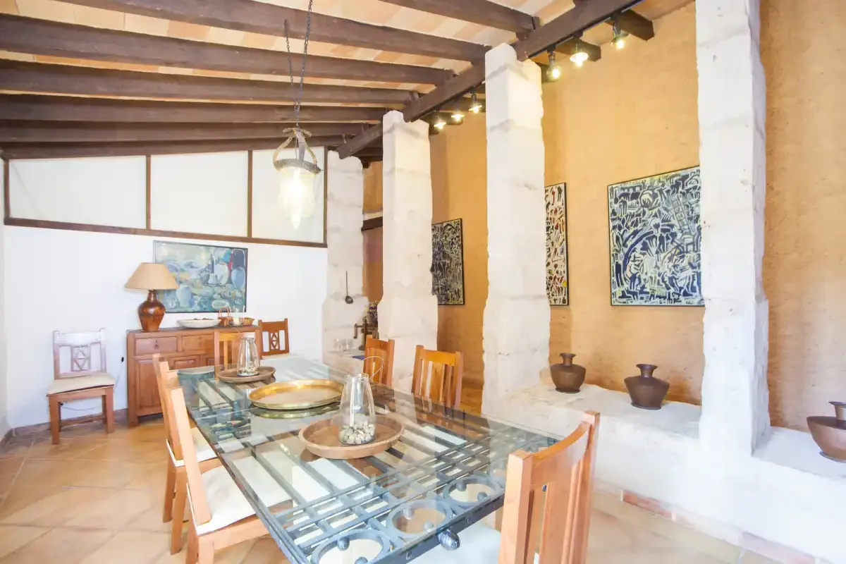 Comedor con una mesa de vidrio y sillas de madera bajo vigas expuestas.