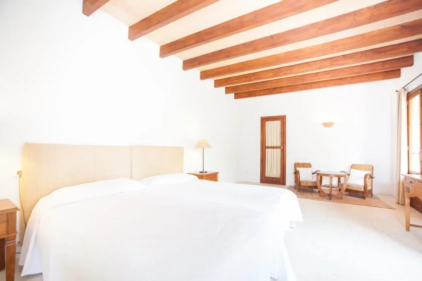 Un dormitorio luminoso con una cama grande y una pequeña zona de estar junto a la ventana.