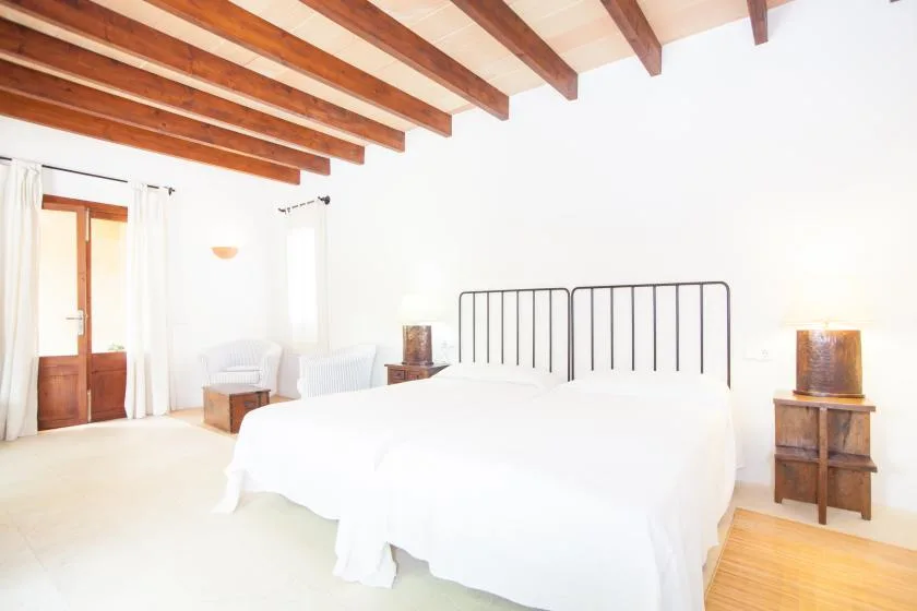 Un dormitorio luminoso con una cama grande, vigas vistas y puertas de madera.
