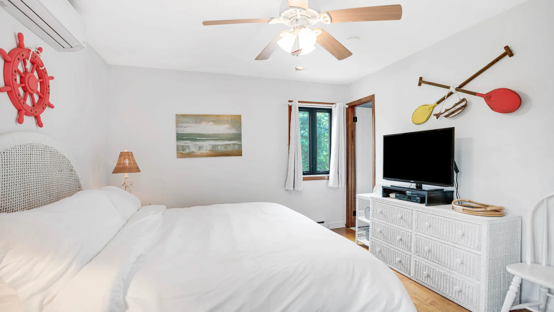 Un dormitorio luminoso con una cama, un televisor y adornos náuticos en la pared.