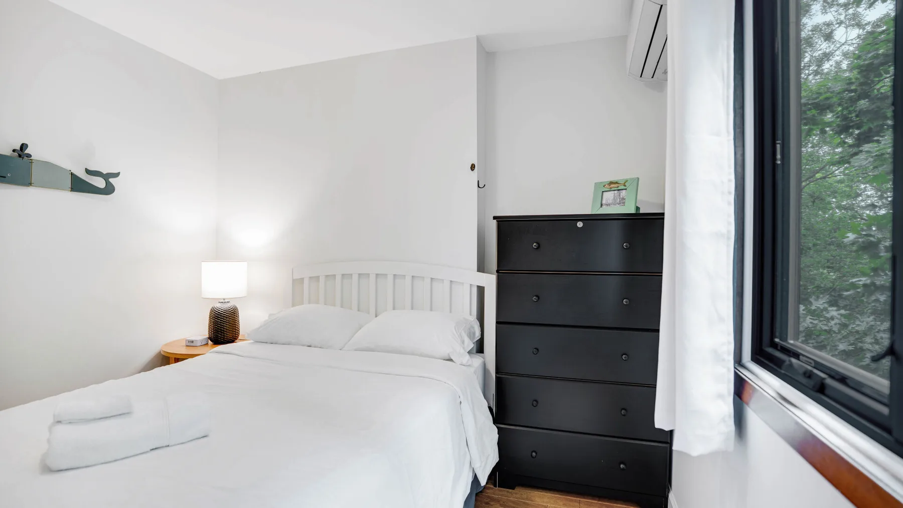 Un dormitorio luminoso con una cama bien hecha y una cómoda oscura.