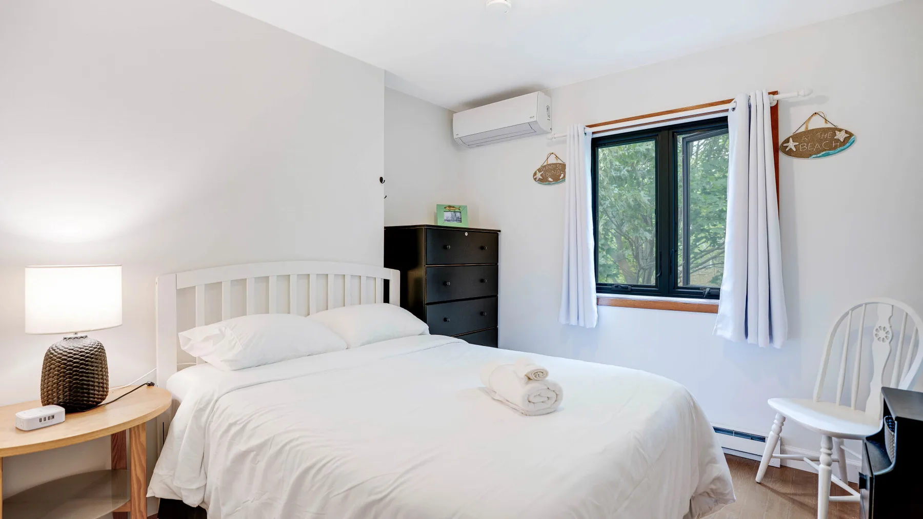 Un dormitorio luminoso con una cama, una cómoda y una ventana con vistas a la vegetación.