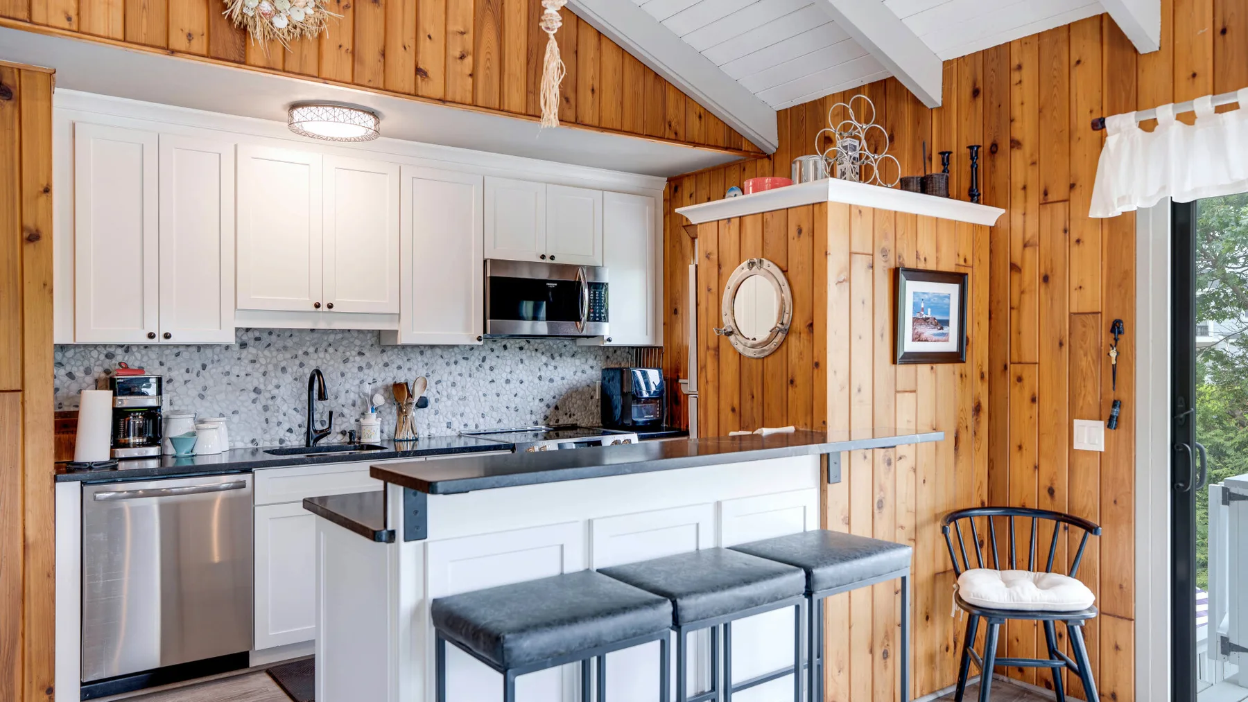 Una cocina luminosa con gabinetes blancos, una encimera y asientos de barra.