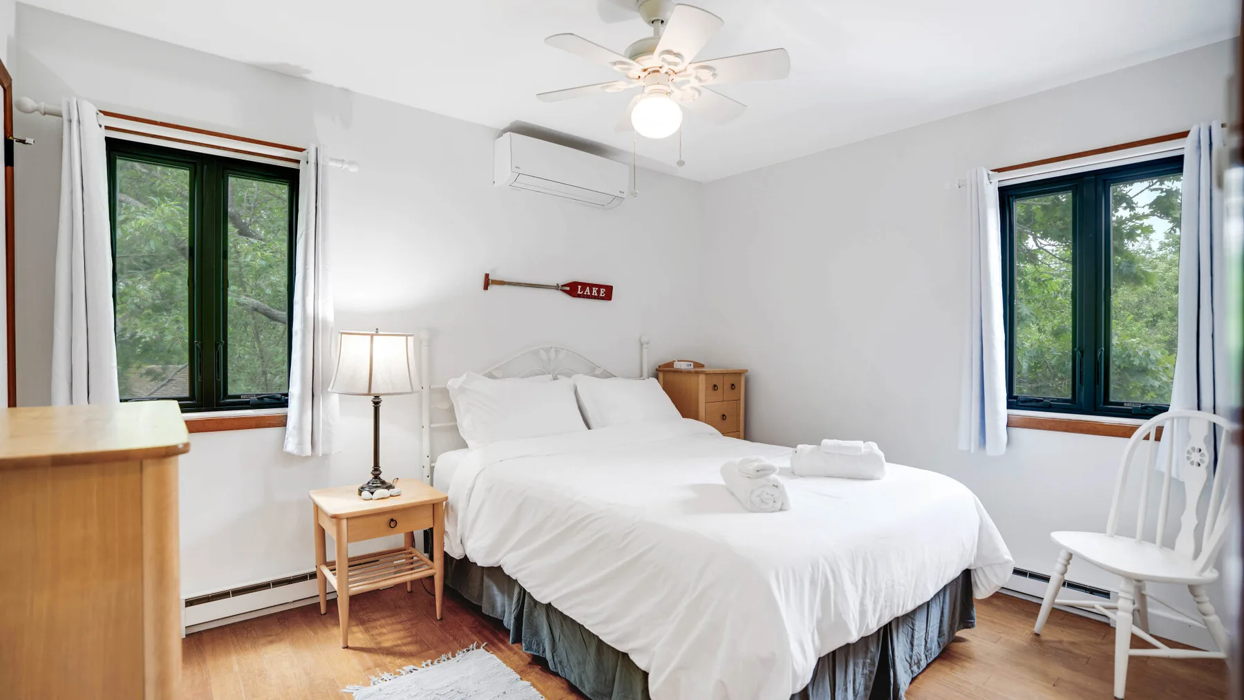 Un dormitorio luminoso con una cama blanca y ventanas en dos paredes.