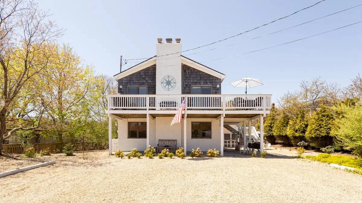 A two-story house with a raised deck and a gravel yard.