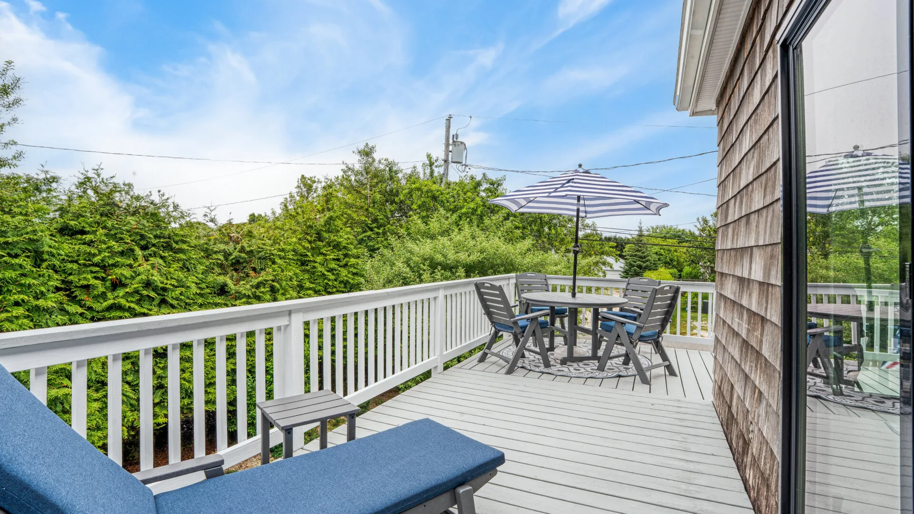 A raised outdoor deck with seating and an umbrella overlooks leafy greenery.