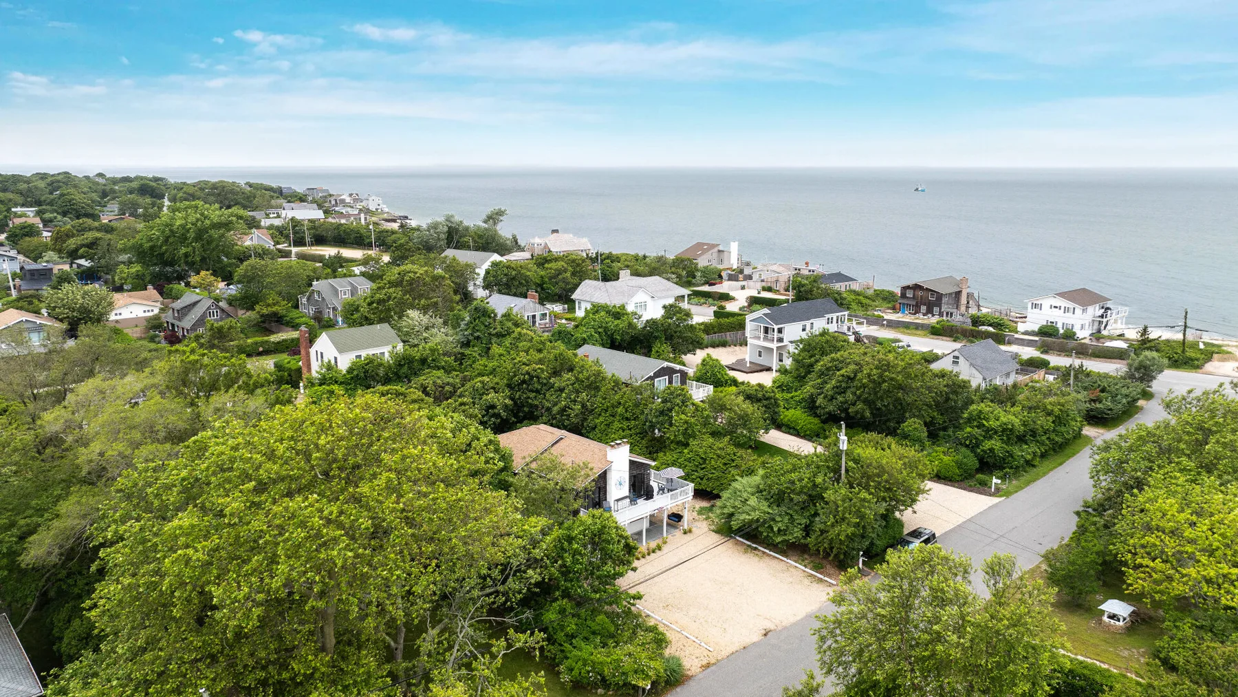 Aerial view of a coastal neighborhood with homes, greenery, and the sea.