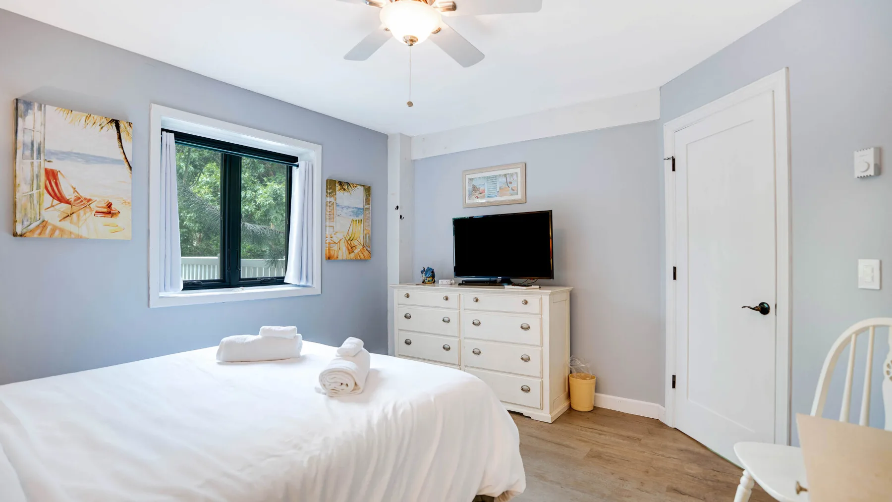 Un dormitorio luminoso con una cama, una cómoda y un televisor.