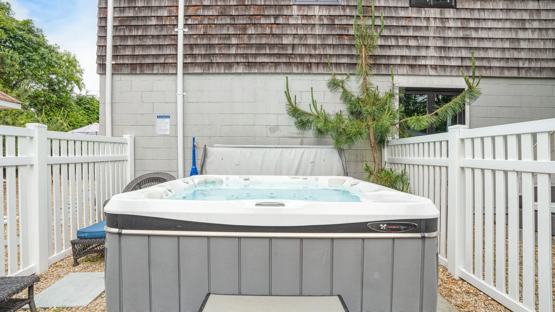 An outdoor hot tub sits between white fences beside a building.