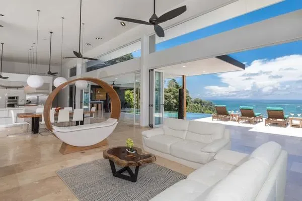Una luminosa sala de estar abierta con asientos blancos y un patio junto a la piscina.